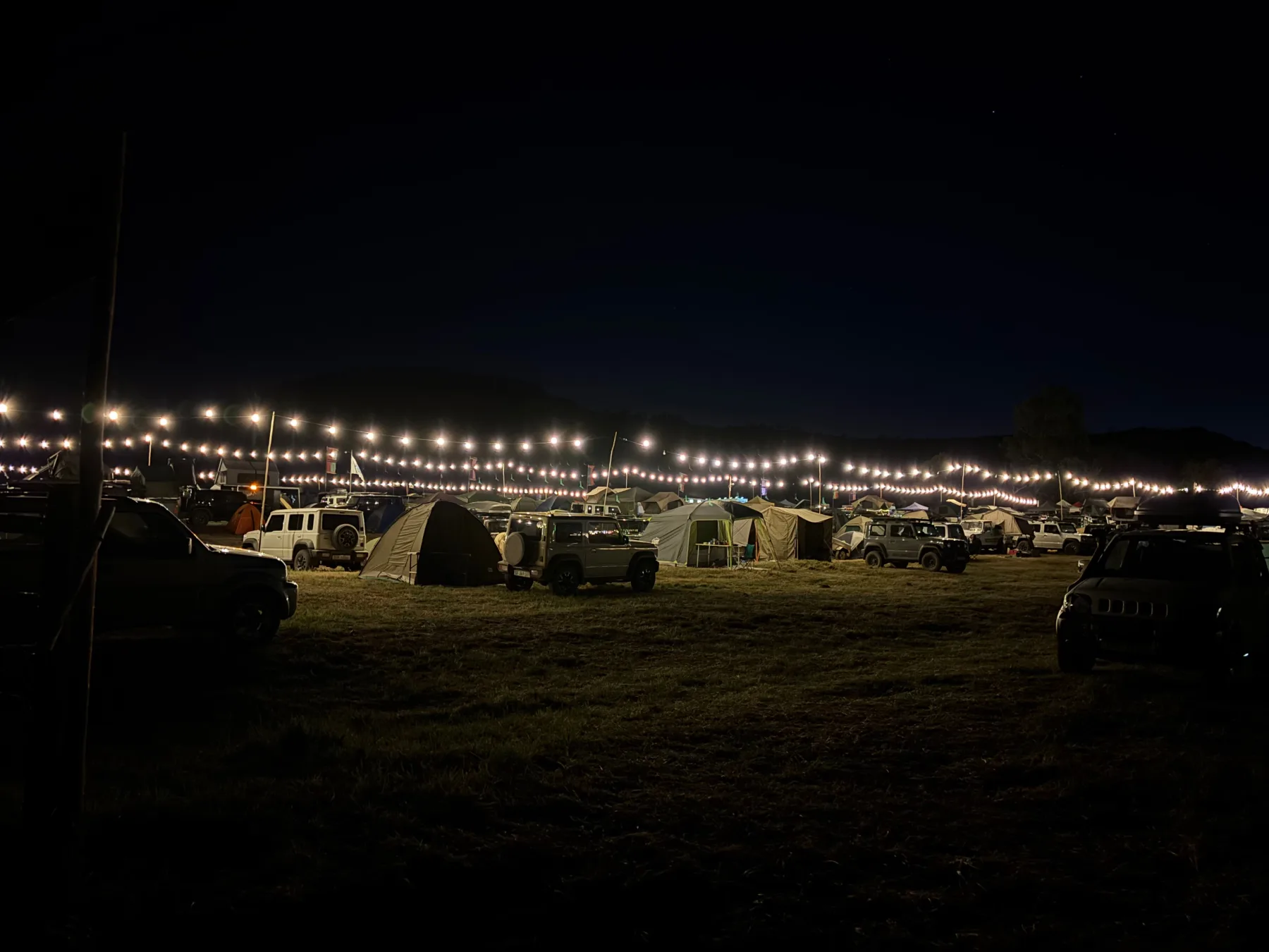 Jimny gathering campsite at night with vehicles, tents and string lights