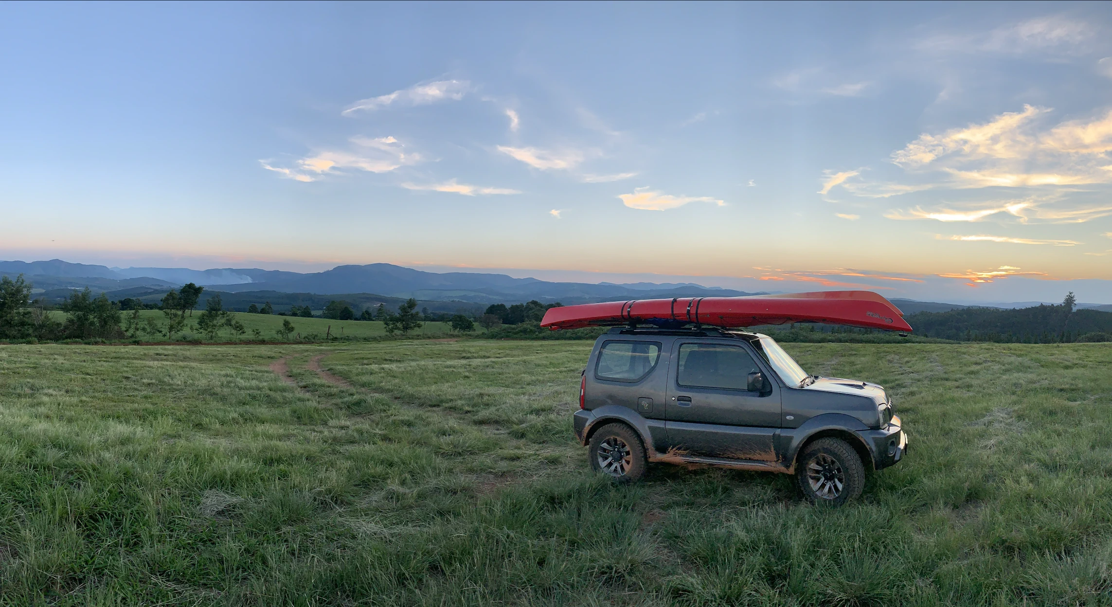 Gen 3 Suzuki Jimny carrying a red kayak in an open field at sunset